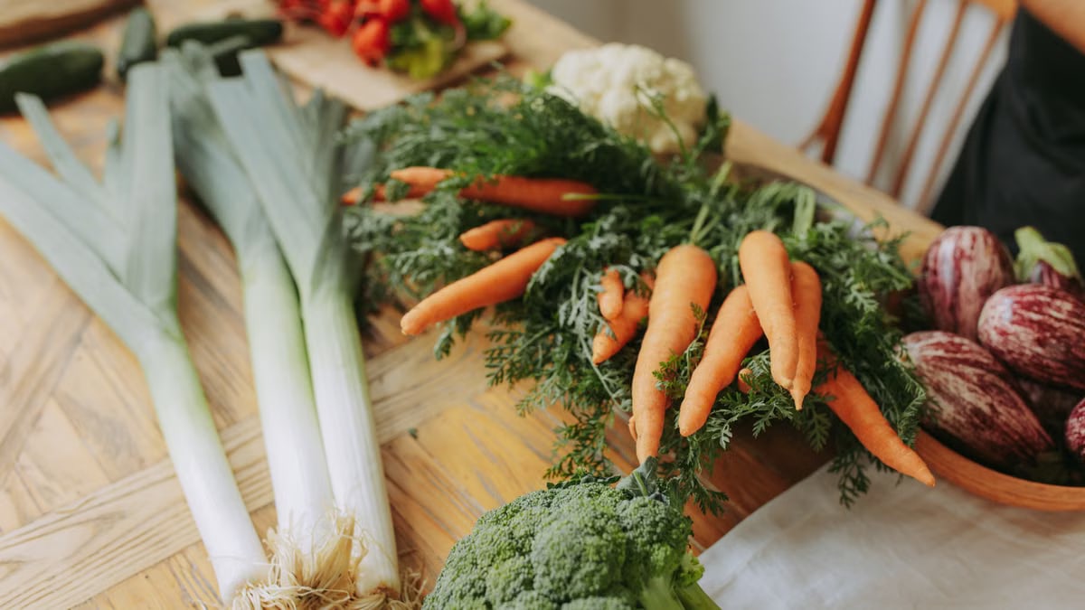 Colorful variety of fresh vegetables including carrots, broccoli, and leeks arranged on a wooden table.